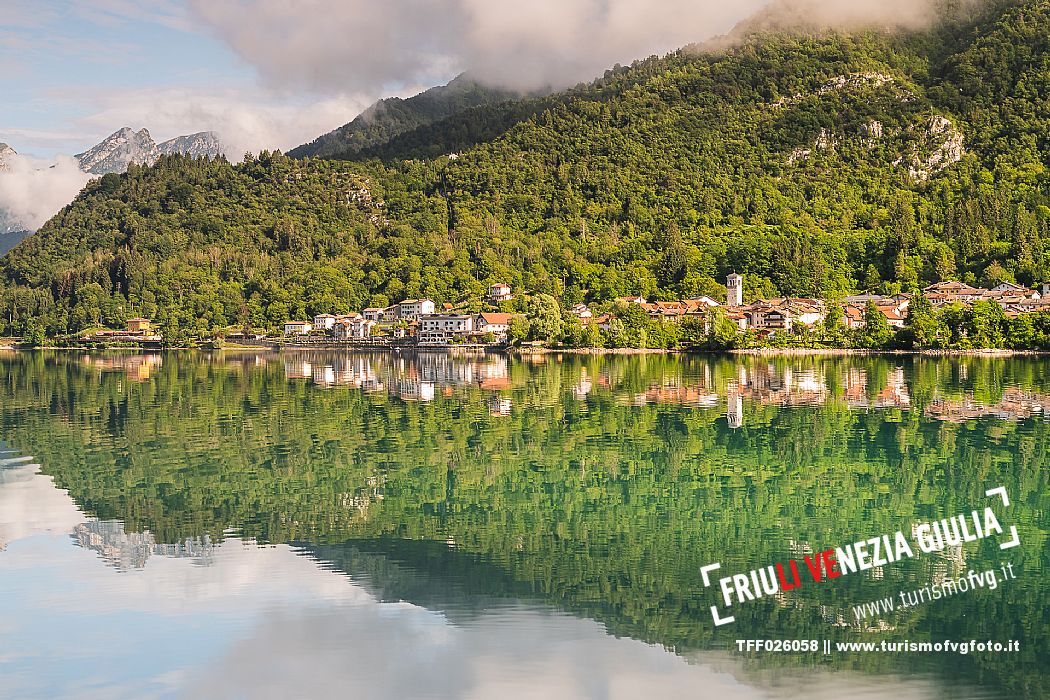 Barcis and its enchanting lake, on a sunny summer morning. In the background the peaks of the Cavallo group and the Friulian Dolomites.