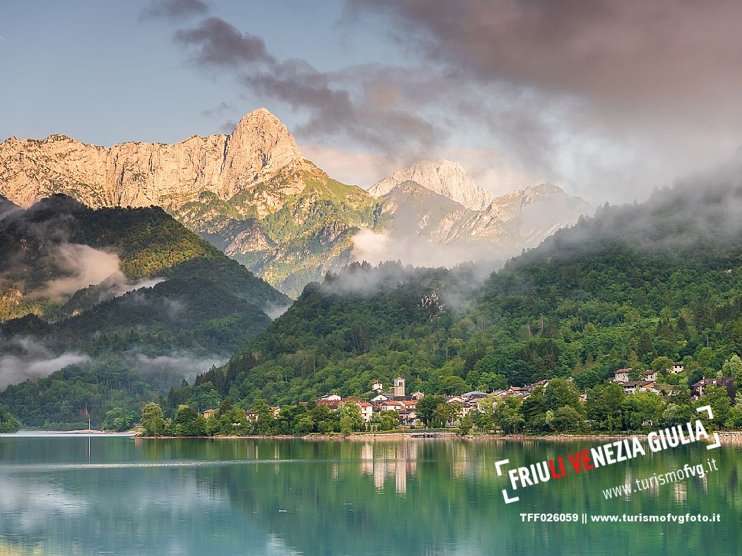 Barcis and its enchanting lake, on a sunny summer morning. In the background the peaks of the Cavallo group and the Friulian Dolomites.