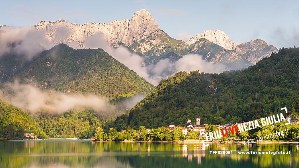 Barcis and its enchanting lake, on a sunny summer morning. In the background the peaks of the Cavallo group and the Friulian Dolomites.