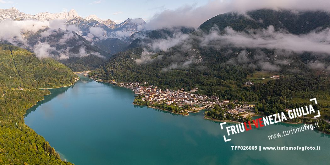 Barcis and its enchanting lake, on a sunny summer morning. In the background the peaks of the Cavallo group and the Friulian Dolomites.