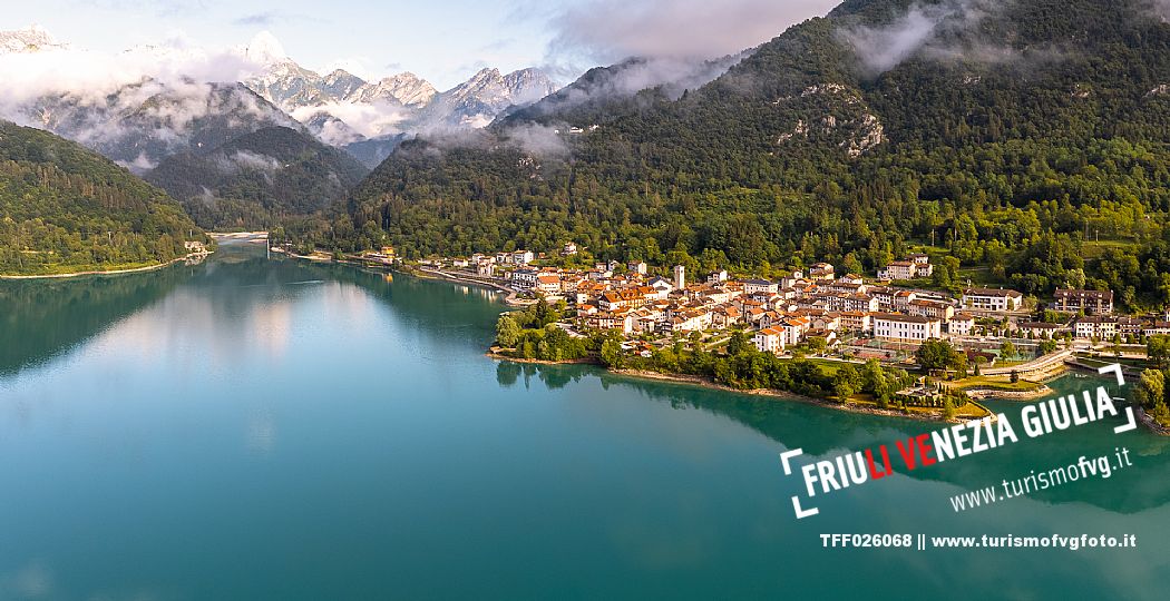 Barcis and its enchanting lake, on a sunny summer morning. In the background the peaks of the Cavallo group and the Friulian Dolomites.