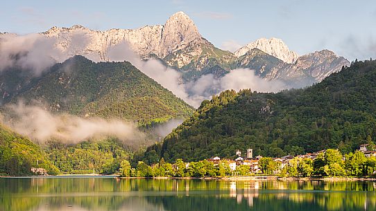 Barcis and its enchanting lake, on a sunny summer morning. In the background the peaks of the Cavallo group and the Friulian Dolomites.