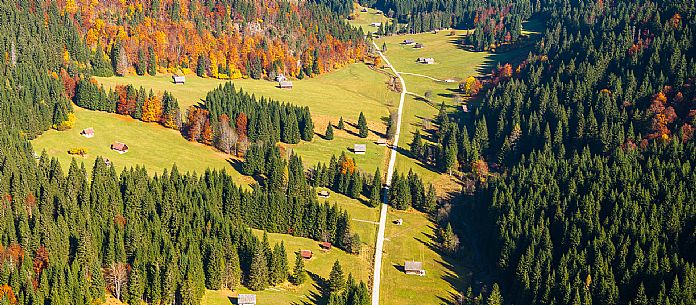 The meadows of Val Bartolo. Here you can immerse yourself in greenery, an expanse of meadows dotted with traditional mountain huts, characterised by wood and sloping roofs with balconies adorned with flowers. Landscapes and trekking in autumn.