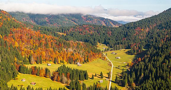 The meadows of Val Bartolo. Here you can immerse yourself in greenery, an expanse of meadows dotted with traditional mountain huts, characterised by wood and sloping roofs with balconies adorned with flowers. Landscapes and trekking in autumn.