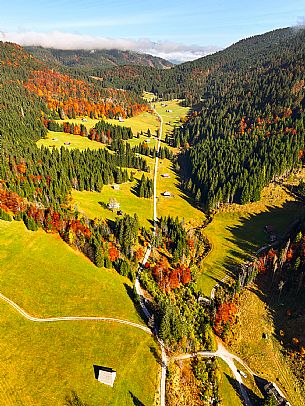 The meadows of Val Bartolo. Here you can immerse yourself in greenery, an expanse of meadows dotted with traditional mountain huts, characterised by wood and sloping roofs with balconies adorned with flowers. Landscapes and trekking in autumn.